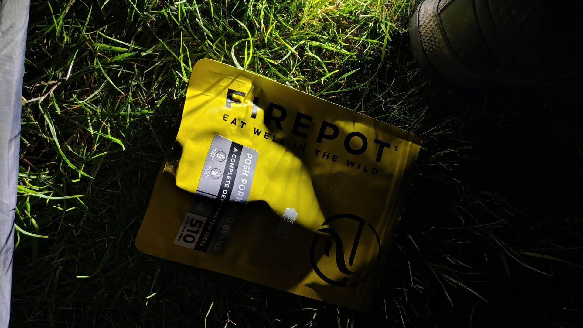 A pouch of Firepot Posh Pork and Beans resting on the grass at a wild camping spot